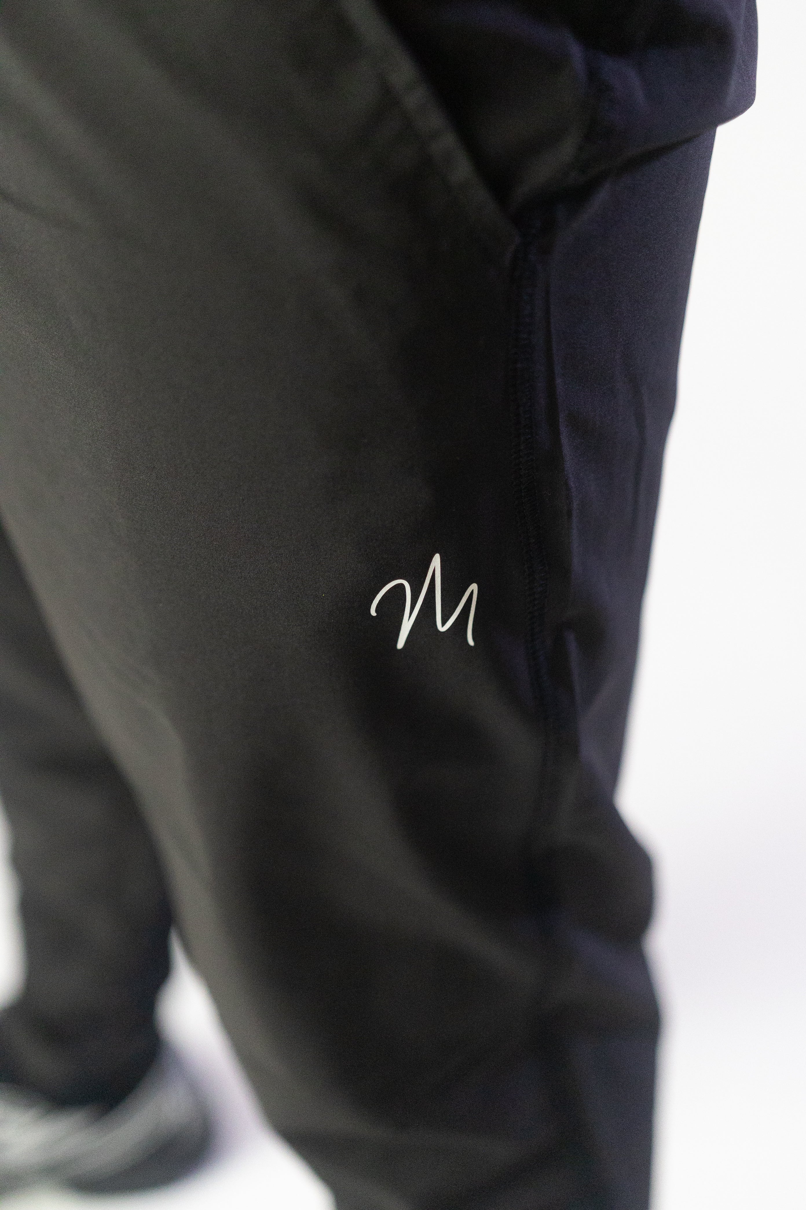 Image du survêtement Stockholm de Mauritti en noir, un ensemble zippé à capuche alliant style sportswear chic et confort. Confectionné en polyester et élasthanne, cet ensemble offre une grande flexibilité et un toucher doux. Il inclut des poches pratiques, une capuche ajustable, une fermeture éclair sur le devant, et des zips aux chevilles pour une touche moderne et fonctionnelle. Parfait pour un look décontracté au quotidien, cet ensemble est aussi adapté aux activités sportives.