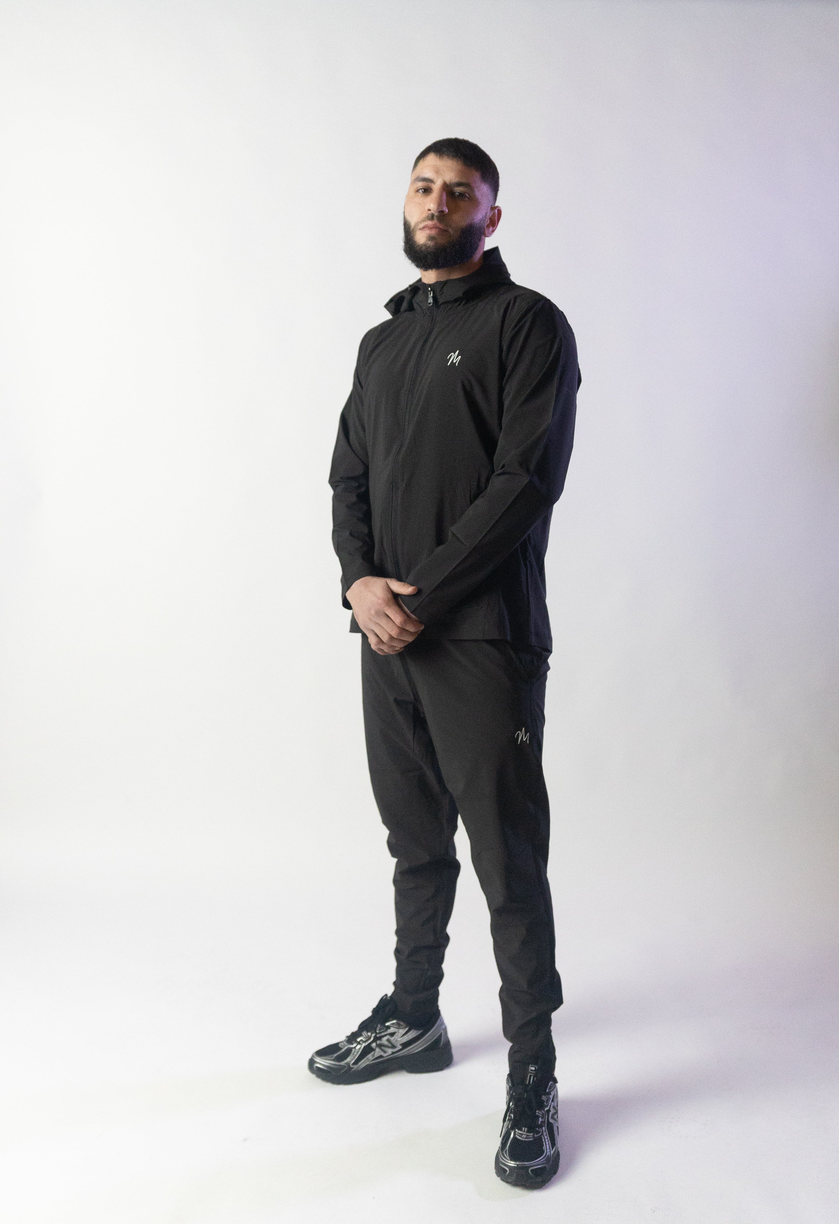Image du survêtement Stockholm de Mauritti en noir, un ensemble zippé à capuche alliant style sportswear chic et confort. Confectionné en polyester et élasthanne, cet ensemble offre une grande flexibilité et un toucher doux. Il inclut des poches pratiques, une capuche ajustable, une fermeture éclair sur le devant, et des zips aux chevilles pour une touche moderne et fonctionnelle. Parfait pour un look décontracté au quotidien, cet ensemble est aussi adapté aux activités sportives.